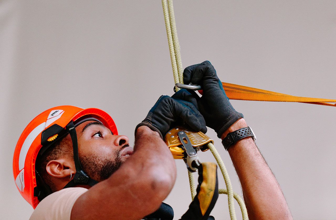 travailleur en hauteur fixant un système de corde avec casque et gants de sécurité